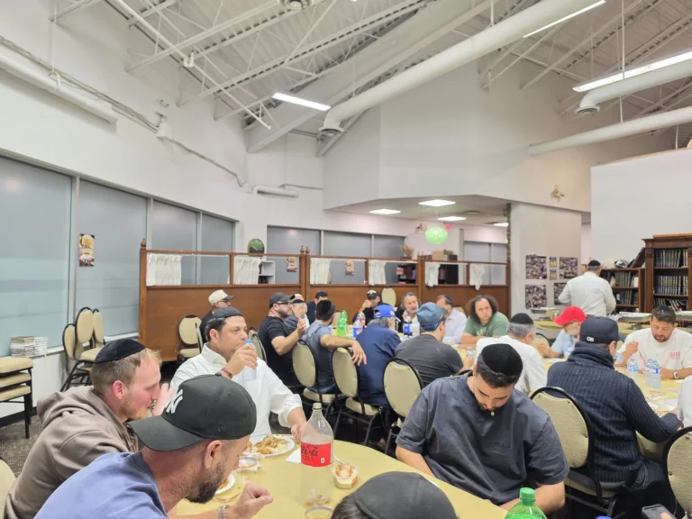 Guests eating together at long tables in the Centre's main hall during a seudah