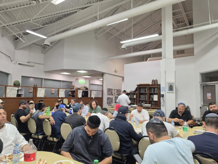A wide view of the main hall full of guests at a seudah
