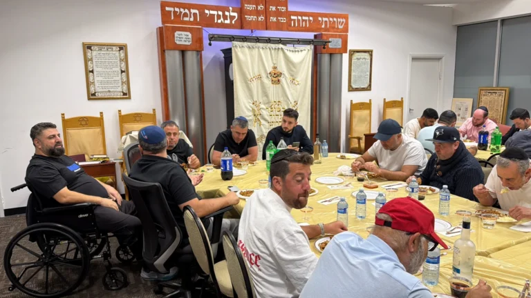 Guests seated around a long table in front of the aron kodesh at a seudah