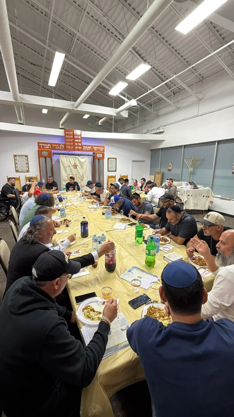 The long table packed with guests at a seudah, seen from one end of the room