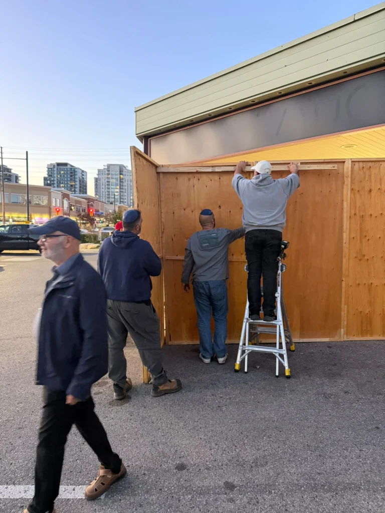 Volunteers fixing a beam across the sukkah walls at dusk