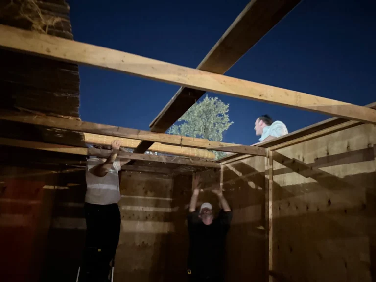Putting the beams for the schach on the Centre's sukkah at night