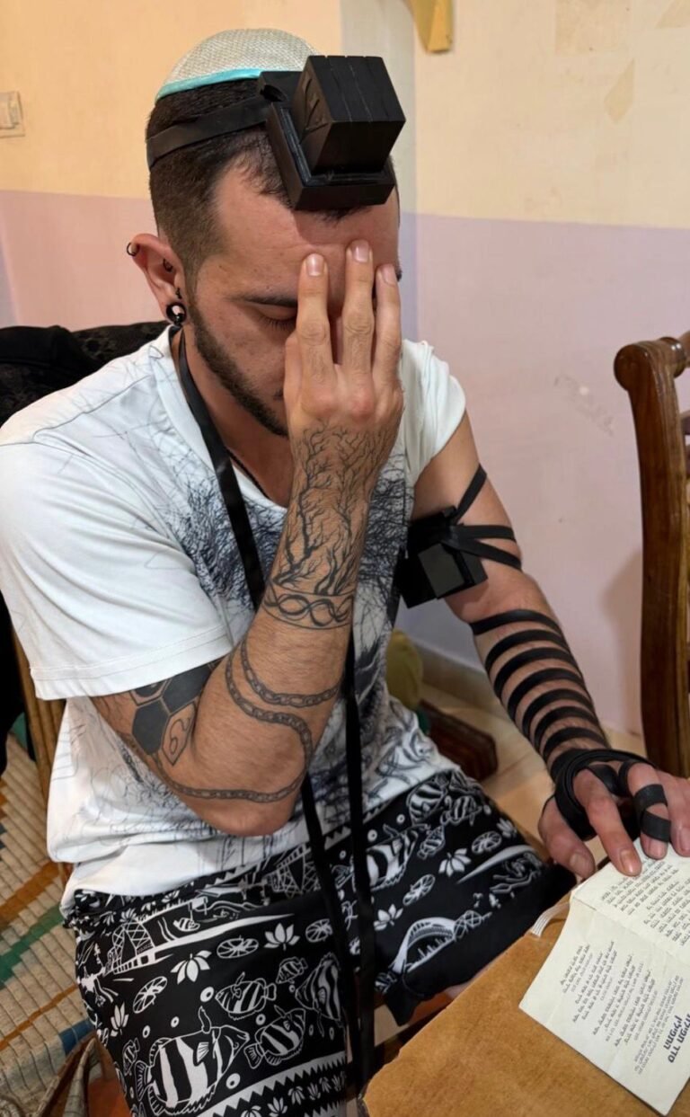A young man in tefillin covering his eyes for the Shema